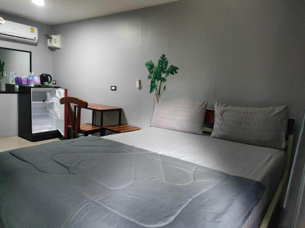 ห้องนอนทันสมัยที่โรงแรมชัยนาทพร้อมเตียงขนาดใหญ่ ชุดเครื่องนอนสีเทา เฟอร์นิเจอร์ไม้ เครื่องปรับอากาศ และไม้ประดับ ที่พักชัยนาท