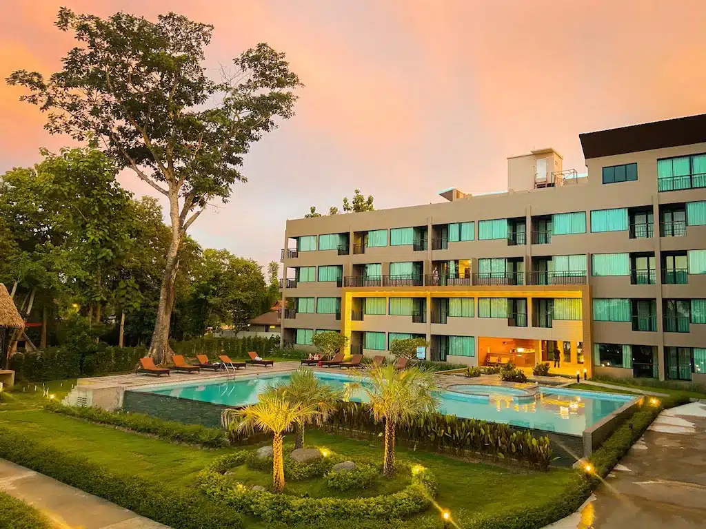 โรงแรมทันสมัยพร้อมสระว่ายน้ำขนาดใหญ่และสวนภูมิทัศน์ยามพลบค่ำ ใต้ท้องฟ้าสีชมพู ตั้งอยู่ริมแม่น้ำโขงในเชียงคาน ที่พักเชียงคานติดริมโขง