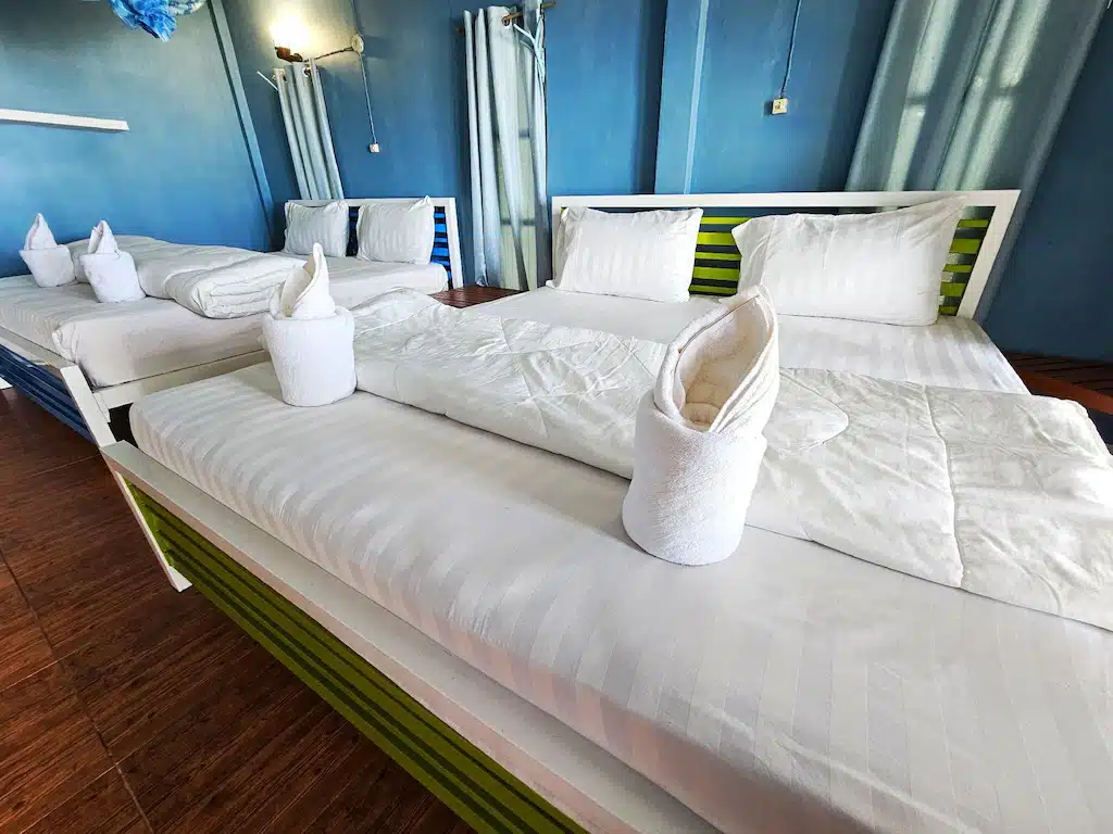 ห้องพักโฮสเทลสว่างสดใสที่เดอะบลูสกายรีสอร์ทเกาะพยามพร้อมเตียงเดี่ยว 4 เตียงประดับด้วยผ้าปูที่นอนสีขาวแล เกาะพยามที่พัก