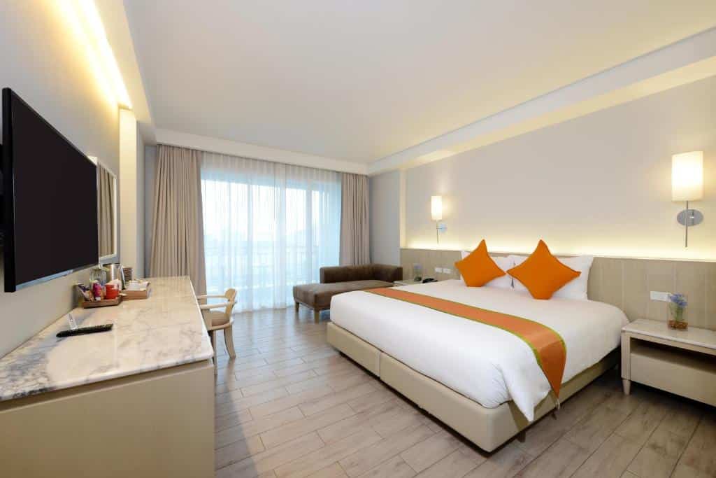 ห้องพักโรงแรมทันสมัยในที่พักหัวหิน พร้อมเตียงขนาดคิงไซส์ ชุดเครื่องนอนสีขาวและสีส้ม ทีวีจอแบนบนผนั ง โรงแรมหัวหิน และบริเวณที่นั่งเล่นใกล้