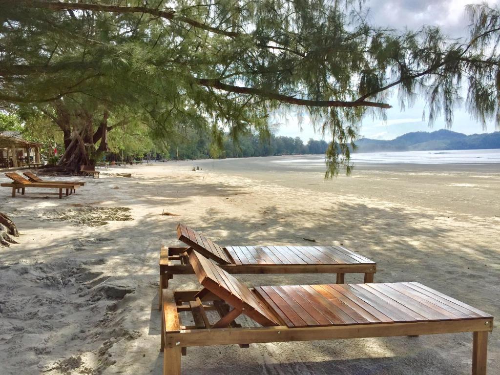 เก้าอี้ไม้บนหาดทรายใต้ต้นไม้อันร่มรื่นที่บลูสกายรีสอร์ทเกาะพยาม พร้อมทิวทัศน์ของ ที่พักเกาะพยาม