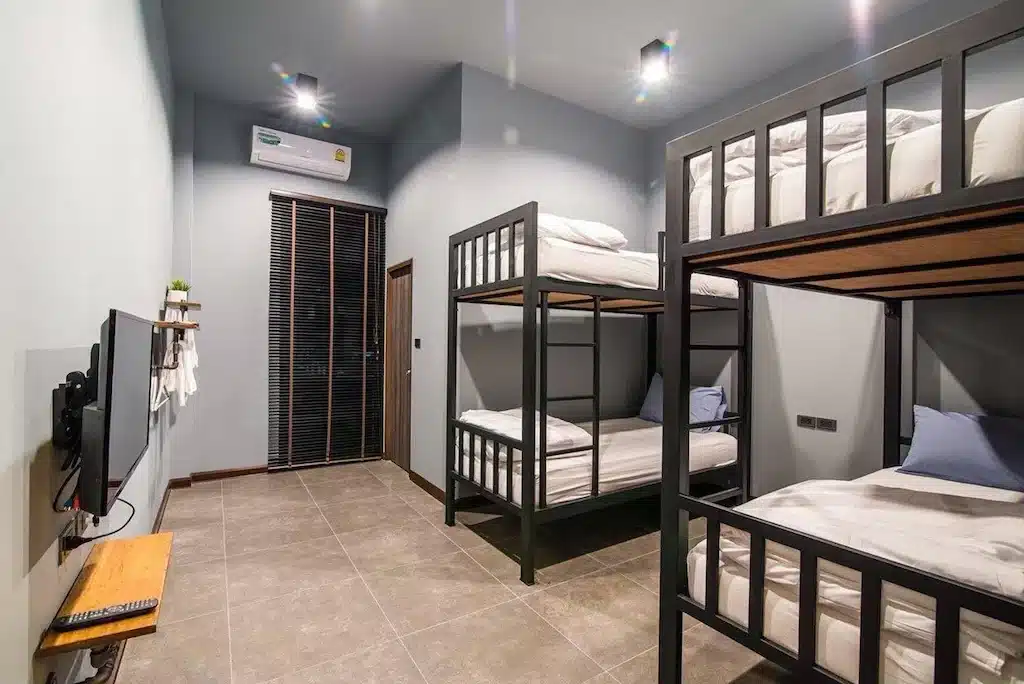 ห้องพักโฮสเทลสไตล์โมเดิร์นผนังสีเทา มีเตียงสองชั้น 2 เตียง พื้นกระเบื้อง เครื่องปรับอากาศ และทีวีจอแบนติดผนังใน ที่พักหัวหิน 