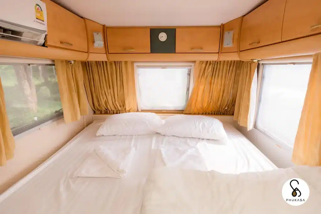 ภายในห้องโดยสารรถไฟอันแสนสบายพร้อมเตียง 2 เตียง ที่พักตาก ผ้าม่านสีส้ม และหน้าต่างที่แสดงทิวทัศน์อันพร่ามัวของการติดต่อตาก