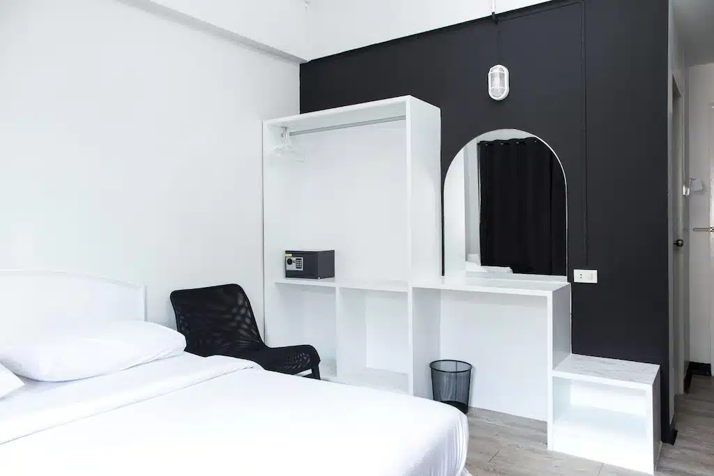 ห้องพักในโรงแรมทันสมัยในหัวหินที่มีเตียงสีขาว ผนังสีดำพร้อมกระจกโค้ง และเก้าอี้สีดำสไตล์มินิมอล รีสอร์ทหัวหิน