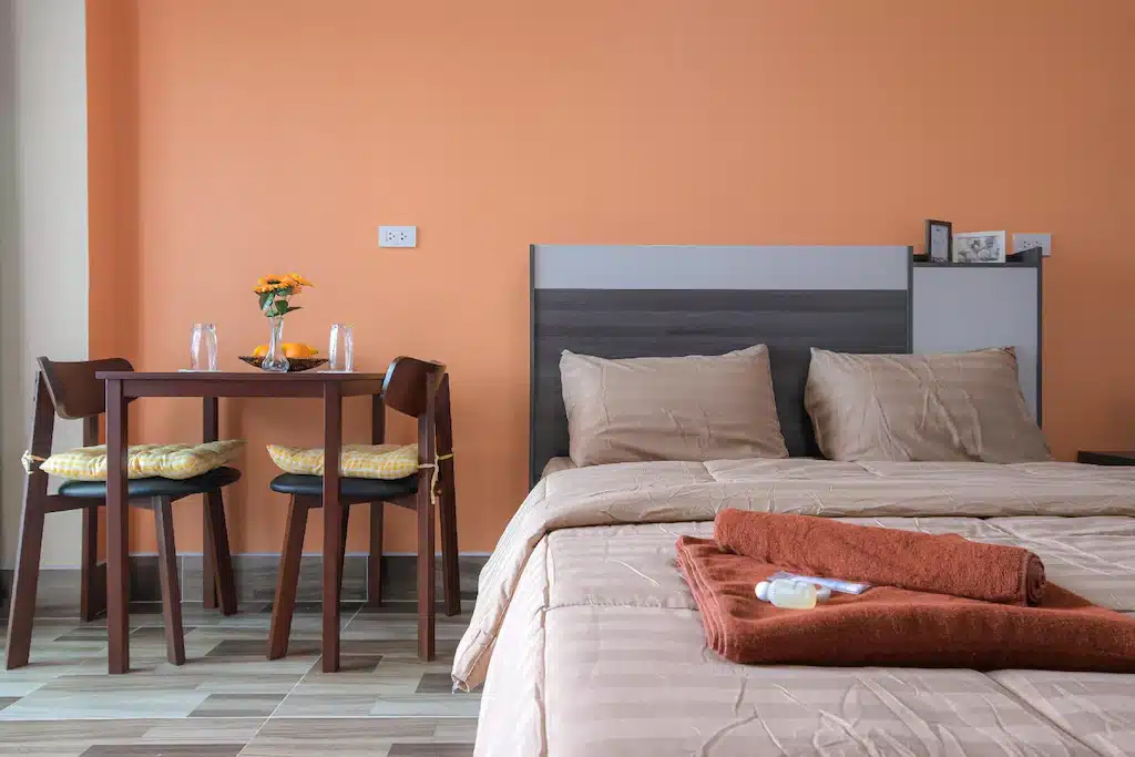 ที่พักแปดริ้ว ห้องนอนทันสมัยพร้อมเตียงคู่และโต๊ะรับประทานอาหารขนาดเล็กสำหรับสองท่าน โดยมีผนังสีส้มอบอุ่นและพื้นไม้ ตั้งอยู่ในสไตล์แปดริ้ว