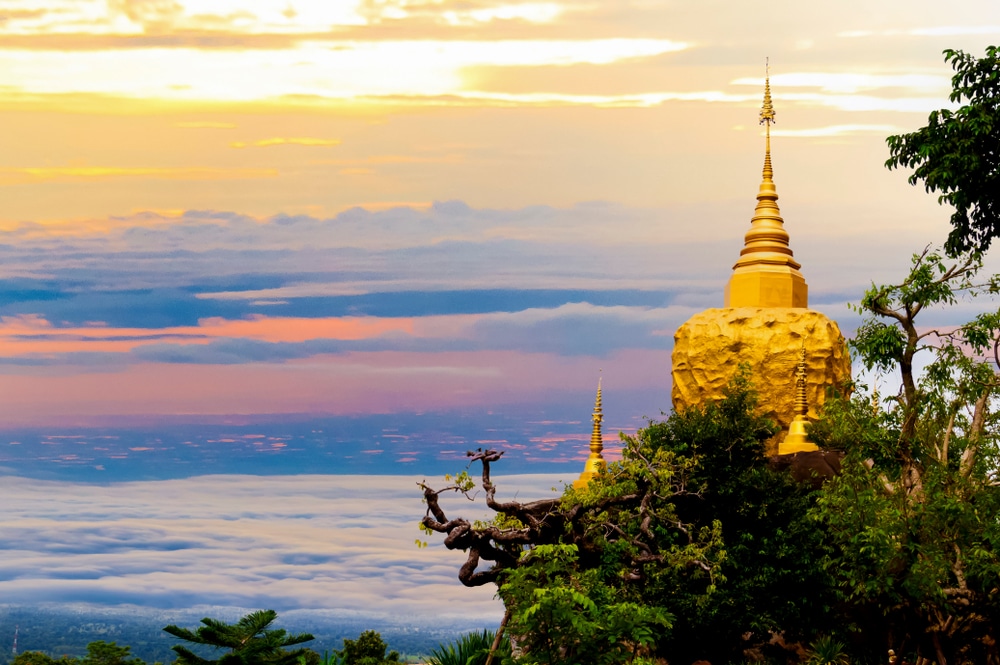 ที่เที่ยวภาคอีสานเจดีย์สีทองบนภูเขาเหนือเมฆยามพระอาทิตย์ตกดินโดยมีท้องฟ้าหลากสีเป็นพื้นหลัง สถานที่ที่โดดเด่นในภาคตะวันออกเฉียงเหนือของประเทศไทย