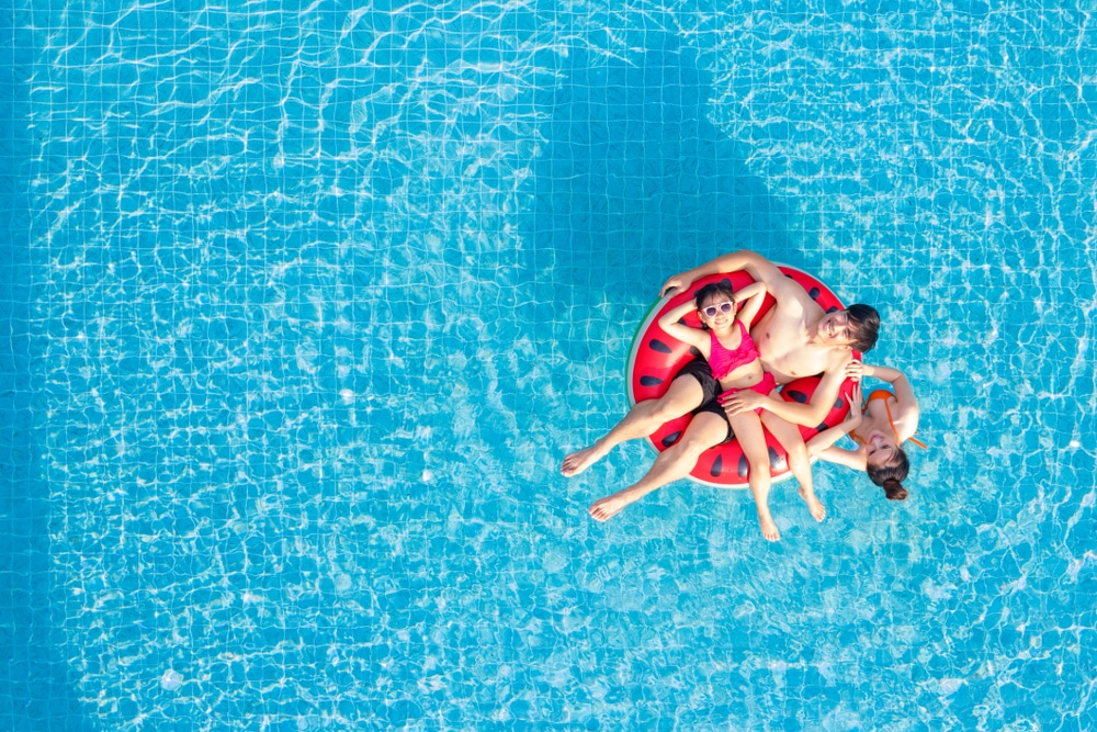 คนสองคนกำลังพักผ่อนบนแตงโมลอยอยู่ในสระว่ายน้ำรีสอร์ทริมทะเลที่เหมาะสำหรับครอบครัว เมื่อมองจากด้านบน