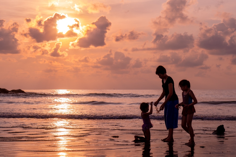 ผู้ใหญ่และเด็กสองคนกำลังเดินไปตามชายหาดตอนพระอาทิตย์ตก เที่ยวเดือนเมษายน