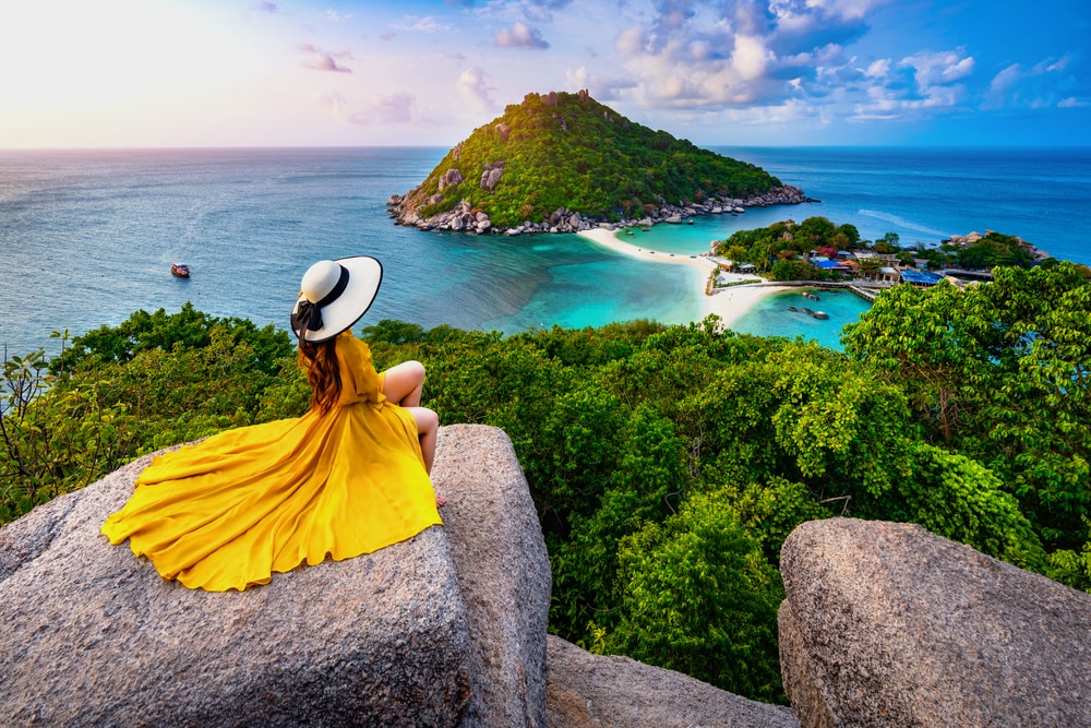ผู้หญิงในชุดสีเหลืองนั่งอยู่บนโขดหินที่มองเห็นเกาะอันงดงามยามพระอาทิตย์ตกดิน เที่ยวเดือนกรกฎาคม ที่เที่ยวเดือนกรกฎาคม