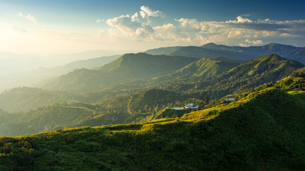 พระอาทิตย์ตกเหนือภูเขาสีเขียวชอุ่มกับหมู่บ้านเล็กๆ ตั้งอยู่บนสันเขา ใต้ท้องฟ้าแจ่มใสที่เต็มไปด้วยทะเลหมอก แนะนำ จุดชมวิว ทะเลหมอก ประเทศไทยสุดว๊าววว ทะเลหมอกยามเช้า อากาศดี บรรยากา