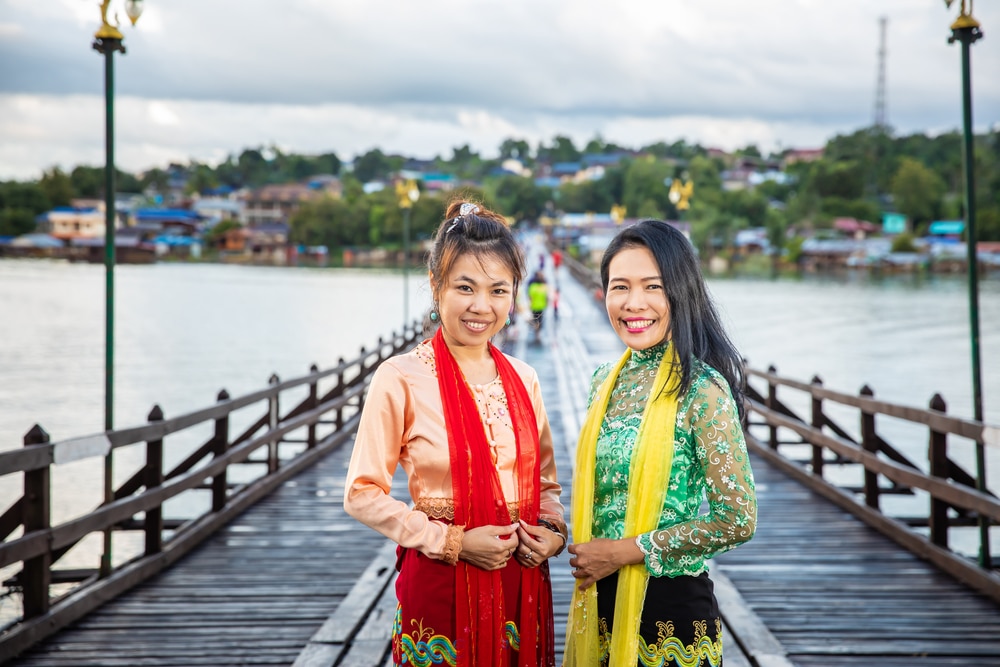 ผู้หญิงสองคนในชุดแบบดั้งเดิมยิ้มบนสะพานไม้ที่มีทิวทัศน์แม่น้ำอันงดงามและที่เที่ยวสาธารณะใน ที่เที่ยวเดือนพฤษภาคม