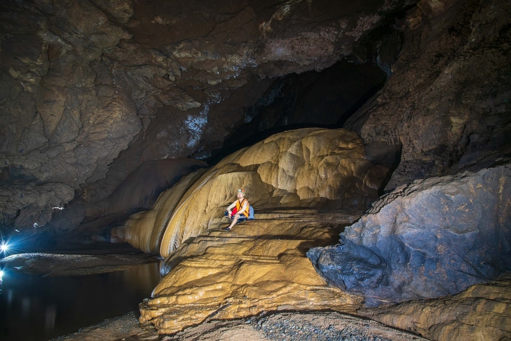 นักสำรวจถ้ำวางอยู่บนภูมิประเทศที่เป็นหินเรียบภายในโพรงถ้ำที่สว่างไสวด้วยแสงประดิษฐ์  ที่เที่ยวเดือนพฤษภาคม ทำให้เป็นสถานที่ในอุดมคติที่เที่ยวเดือนพฤษ