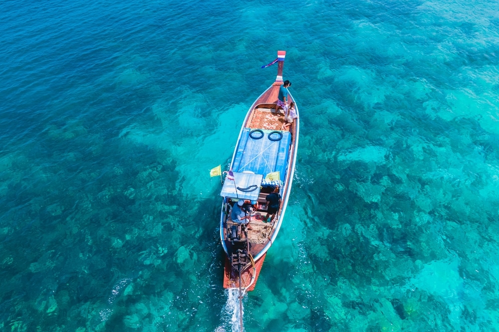 มุมมองทางอากาศของเรือหางยาวที่ลอยอยู่ในน้ำทะเลสีฟ้าครามใสใกล้เกาะที่สวยที่สุดในโลกเมื่อมองจากด้านบน เกาะที่สวยที่สุดในโลก
