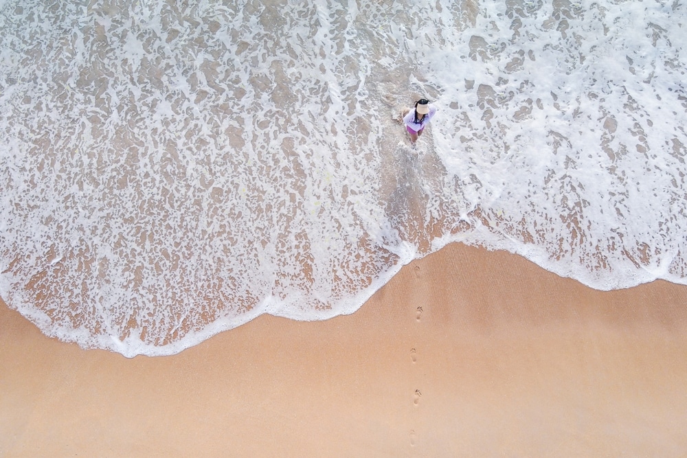 มุมมองทางอากาศของคนยืนอยู่บนหาดทรายที่มีคลื่นซัดเข้ามาใกล้เท้า เหมาะสำหรับที่ เที่ยวเดือนเมษายน