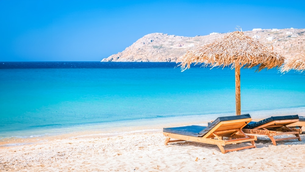 เก้าอี้เลานจ์สองตัวใต้ร่มฟางบนหาดทรายที่มีน้ำทะเลสีฟ้าใสและเนินเข เกาะที่สวยที่สุดในโลก าหินบนเกาะในประเทศในโลก