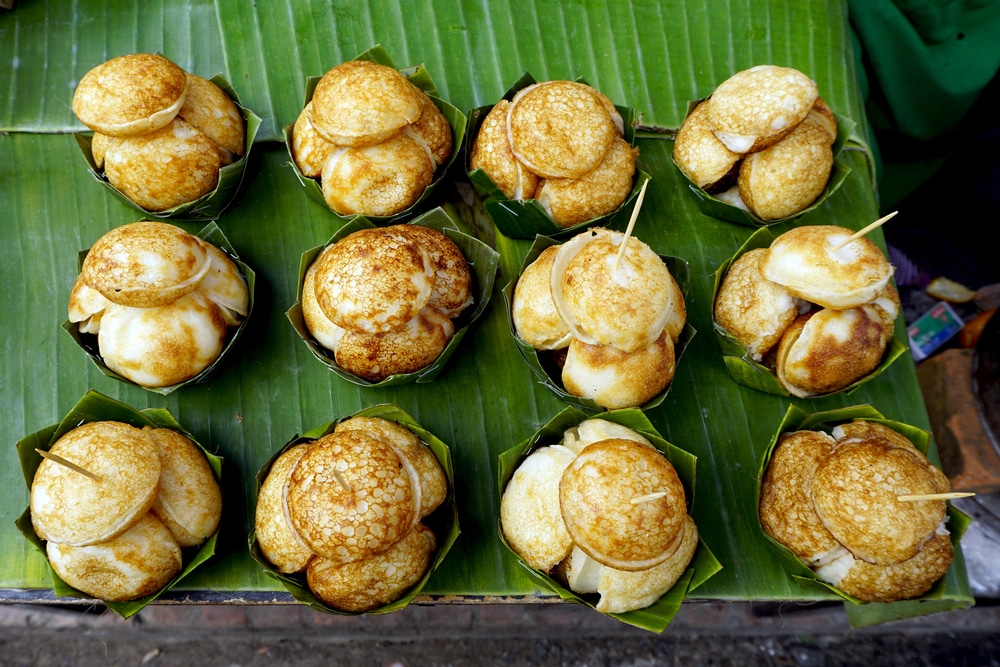 ขนมครกเป็นแถว แพนเค้กมะพร้าวไทย เสิร์ฟในชามใบตองสีเขียว ที่เที่ยวหลวงพระบาง  บนโต๊ะตลาดในราชบุรี