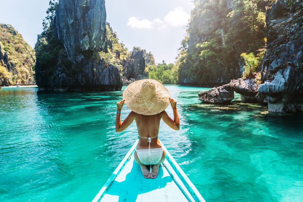 ผู้หญิงสวมหมวกฟางยืนอยู่ที่หัวเรือ มองเห็นทะเลสาบสีฟ้าครามอันเงียบสงบบนเกาะในโล เกาะที่สวยที่สุดในโลก