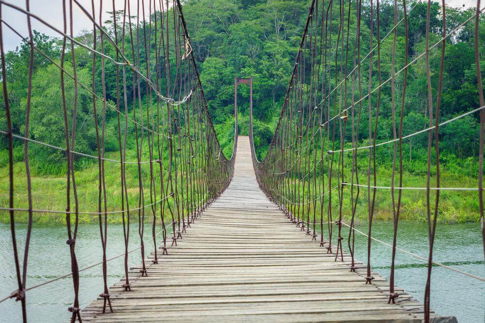 สะพานเชือกแขวนที่ทอดยาวข้ามแม่น้ำท่ามกลางแมกไม้เขียวขจี ที่เที่ยวเดือนพฤษภาคม ที่เที่ยวสาธารณะ