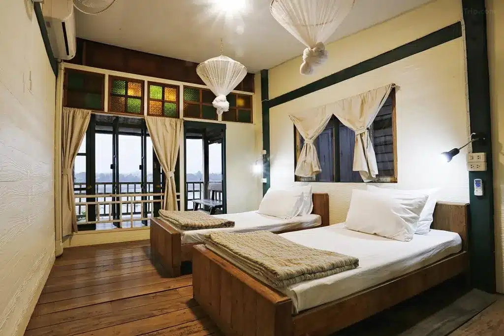 ห้องพักในโรงแรมแสนสบายพร้อมเตียงแฝด 2 เตียง ที่พักเชียงคานราคาถูก แต่ละเตียงมีผ้านวมสีขาวและผ้าเช็ดตัวพับอยู่ที่ปลายเตียง คุณสมบัติเชียงคานมีพื้นไม้ หน้าต่างกระจกสี และระเบียงที่เข้าถึงได้ผ่านประตูกระจก เหมาะสำหรับผู้ที่มาเยือนพื้นที่ท่องเที่ยวน่านในบริเวณใกล้เคียง