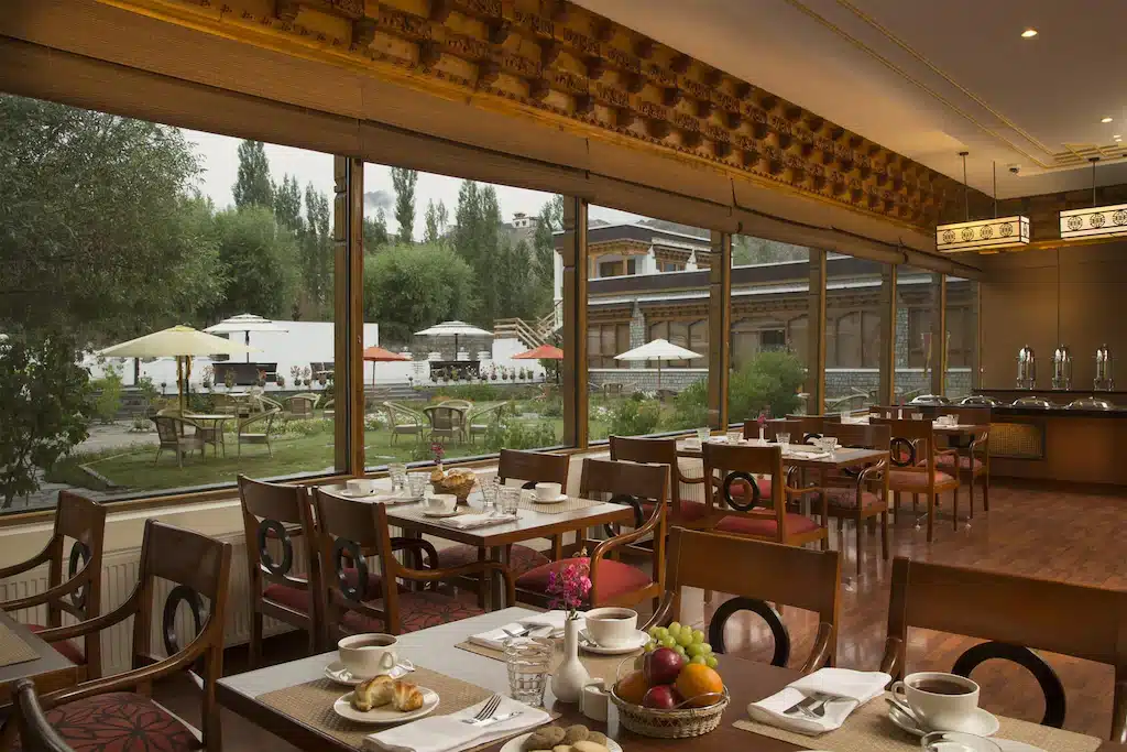 ภายในร้านอาหารของโรงแรมอันกว้างขวางในราชบุรีพร้อมโต๊ะสำหรับมื้อเช้า หน้าต่างบานใหญ่มองเห็นระเบียงสวน