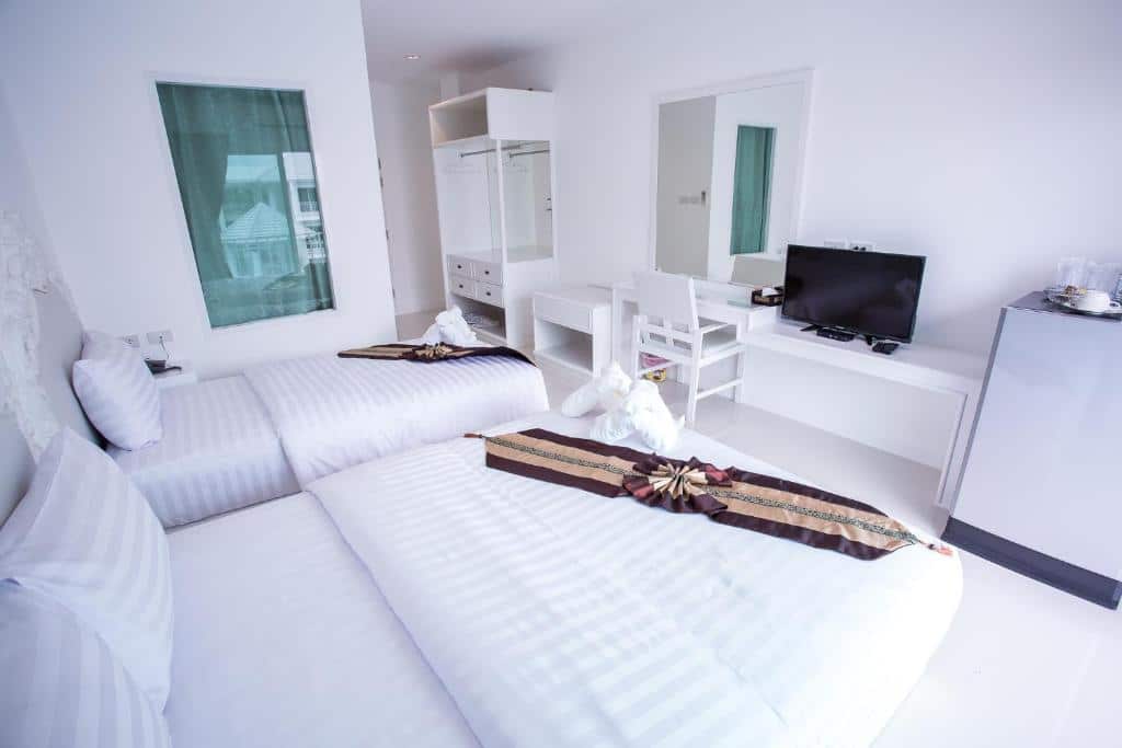 ห้องพักในโรงแรมสีขาวสว่างสดใสพร้อมเตียงแฝดที่ตกแต่งอย่างประณีต 2 เตียง ทีวีจอแบนบนโต๊ะ ตู้เย็นขนาดเล็ ก ที่พักอุ้มผาง และตู้เสื้อผ้า หน้าต่างพร้อมผ้าม่านโปร่งช่วยเพิ่มแสงธรรมชาติให้กับห้อง