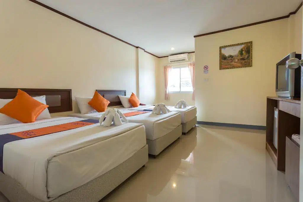 ห้องพักในโรงแรมที่มีอ่างขางมีเตียงเดี่ยว 3 เตียงตกแต่งด้วยชุดเครื่องนอนสีส้มและสีขาว โต๊ะไม้พร้อมทีวี หน้าต่างพร้อมม่านปรับแสง และภาพวาดที่มีกรอบบนผนัง ดอยอ่างข่างที่พัก