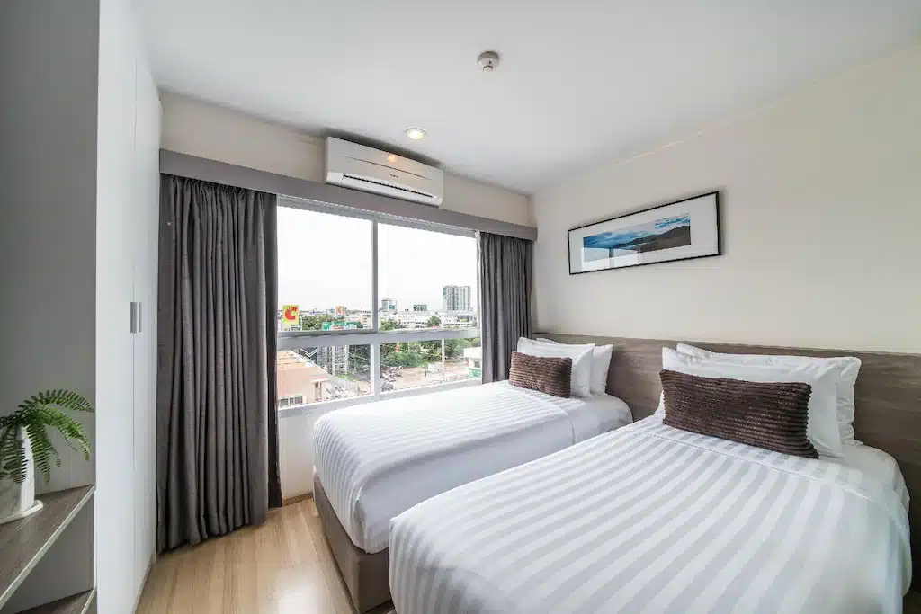 ห้องพักในโรงแรมทันสมัยพร้อมเตียงแฝด 2 เตียง ผ้าปูที่นอนสีขาว ผ้าม่านสีเข้ม และวิวเมืองที่สวยงามผ่านหน้าต่าง ที่พักพัทยา