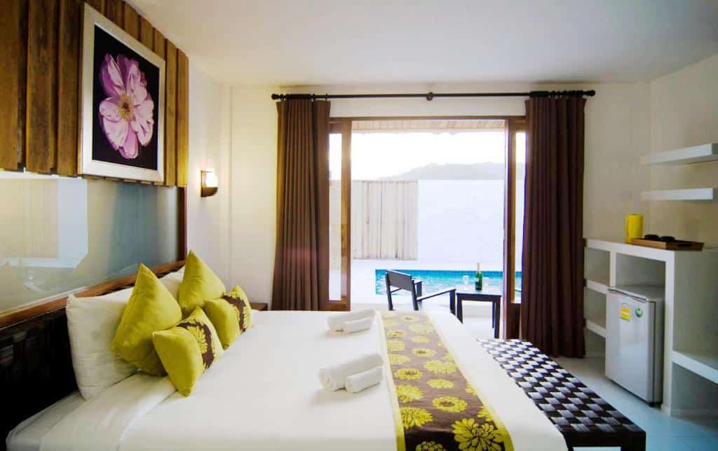 ห้องพักในโรงแรมที่มีเตียงขนาดใหญ่ประดับด้วยหมอนสีเหลืองและสีเขียว มีสระว่ายน้ำที่มองเห็นได้จากหน้าต่าง และการตกแต่งที่เรียบง่าย ตั้งอยู่ริมทะเลในปราณบุรี