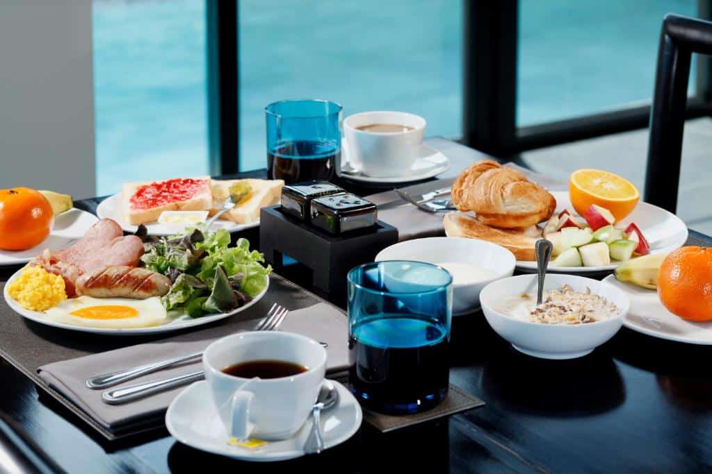 อาหารเช้าวางบนโต๊ะข้างหน้าต่างพูลวิลล่าในภูเก็ต โดยมีจานประกอบด้วยไข่ เบคอน สลัด ครัวซองต์ ผลไม้ กาแฟ และน้ำผลไม้