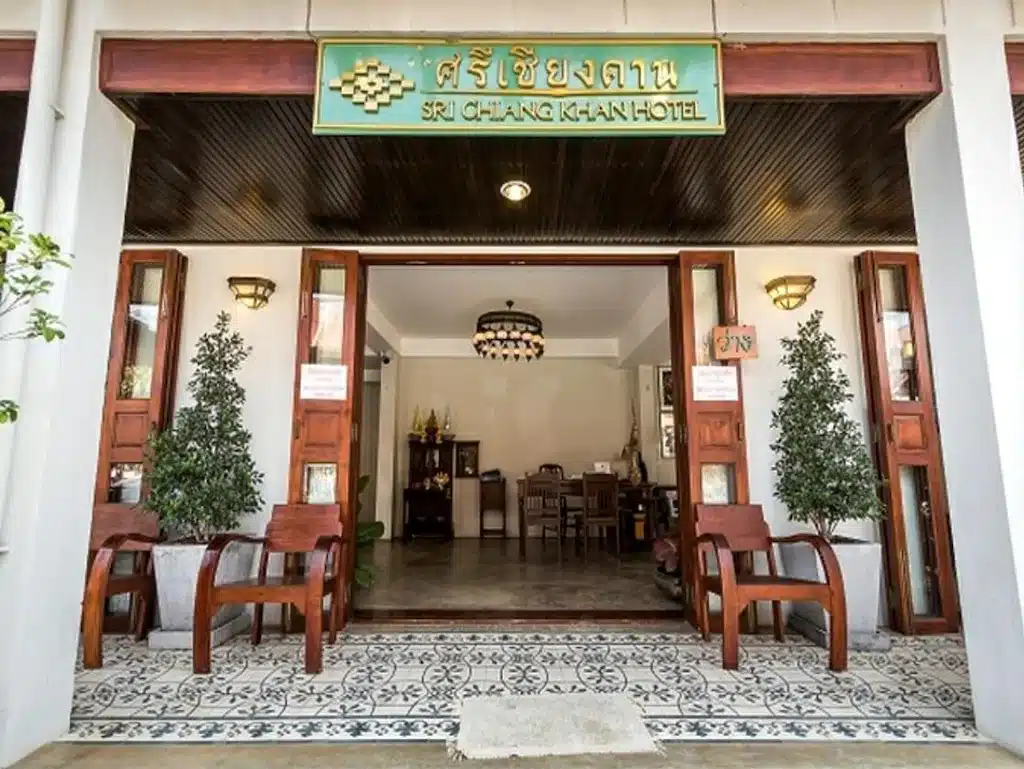         ทางเข้าโรงแรมศรีเชียงคานมีเก้าอี้ไม้และกระถางต้นไม้อยู่สองข้าง มีโคมระย้ามองเห็นด้านใน และชื่อโรงแรมเขียนเป็นภาษาไทยและอังกฤษเหนือทางเข้าประตู  โรงแรมเชียงคาน เพลิดเพลินกับการเข้าพักที่เชียงคานขณะสำรวจสถานที่ท่องเที่ยวน่านในบริเวณใกล้เคียง