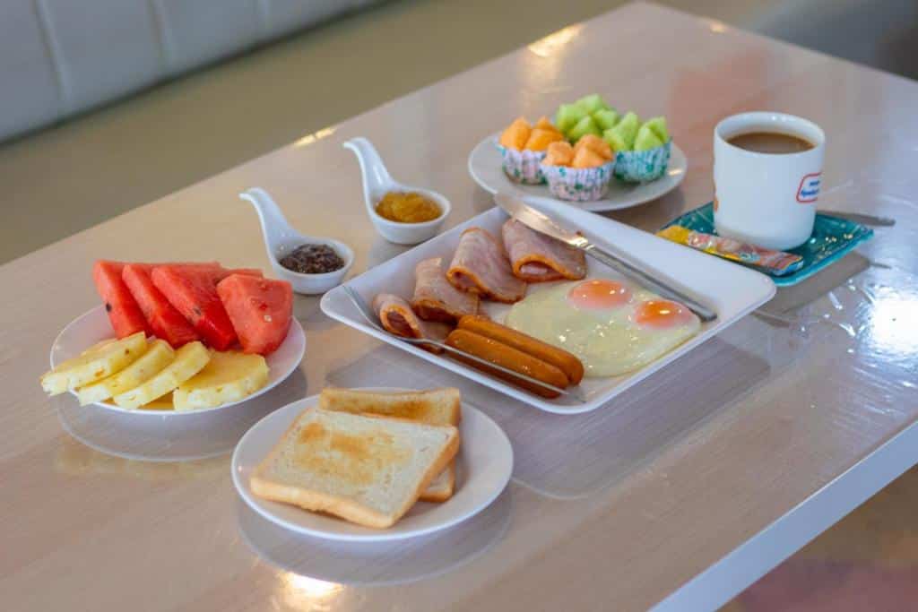 อาหารเช้าที่โรงแรมบางสะพานประกอบด้วยขนมปังปิ้ง ไข่แดดเดียว ไส้กรอก เบคอน ผลไม้นานาชนิด กาแฟ และเครื่องปรุงรสบนโต๊ะที่จัดอย่างสวยงาม ที่พักบางสะพาน