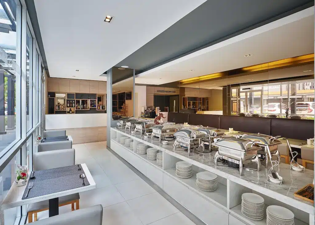 พื้นที่บุฟเฟ่ต์โรงแรมทันสมัยพร้อมอาหารจานเนื้อ จานซ้อน และที่นั่ง มองเห็นวิวถนนในเมืองผ่านหน้าต่างบานใหญ่ในไอคอนน ที่พักพัทยา