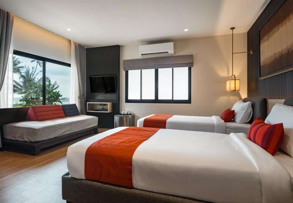 ห้องพักโรงแรมทันสมัยที่โรงแรมบางสะพานมีเตียงแฝด 2 เตียง โซฟา ทีวีจอแบน หน้าต่างบานใหญ่ และเครื่องนอนสีแดงและสีขาว ที่พักบางสะพาน
