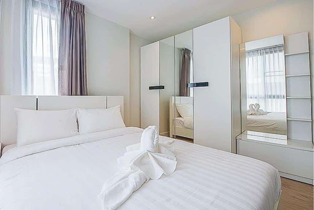 ห้องนอนทันสมัยสว่างสดใสพร้อมผ้าปูที่นอนสีขาวบนเตียง ตู้เสื้อผ้ากระจก และโต๊ะเครื่องแป้งพร้อมกระจก ที่พักอุ้มผาง