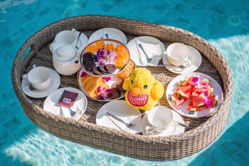 ถาดอาหารเช้าลอยน้ำพร้อมของเล่นตุ๊กตาสีเหลือง จานผลไม้ และชุดน้ำชาในสระว่ายน้ำที่พูลวิลล่าสำหรับครอบครัวในภูเก็ตในราคาประหยัด
