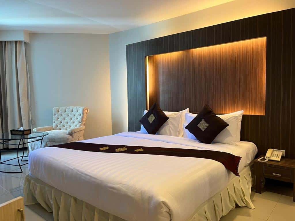 ห้องพักโรงแรมทันสมัยในโรงแรมฉะเชิงเทราพร้อมเตียงคู่ขนาดใหญ่ ชุดเครื่องนอนสีขาวและสีแดง หัวเตียงมีไฟแบ็คไลท์ และพื้นที่นั่งเล่นพร้อมเก้าอี้เท้าแขนสีขาว ที่พักฉะเชิงเทรา