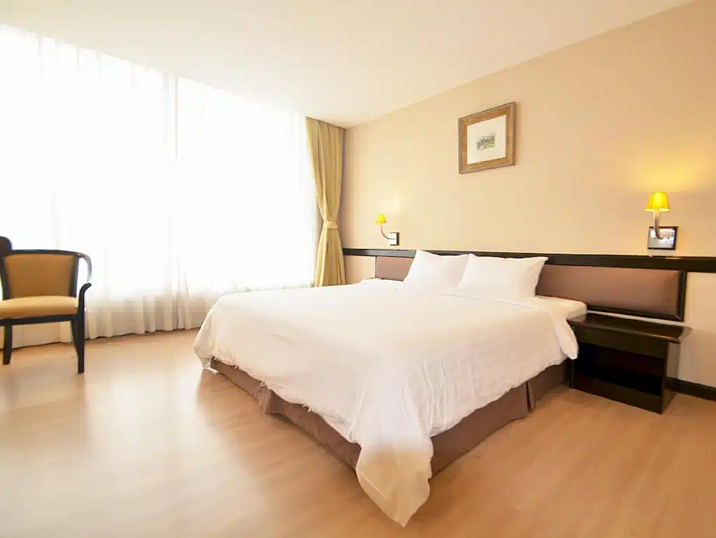 ห้องพักในโรงแรมที่มีแสงสว่างเพียงพอในโรงแรมศรีราชาติดทะเลมีเตียงคู่พร้อมชุดเครื่องนอนสีขาวเป็นไม้ ที่พักศรีราชาติดทะเล