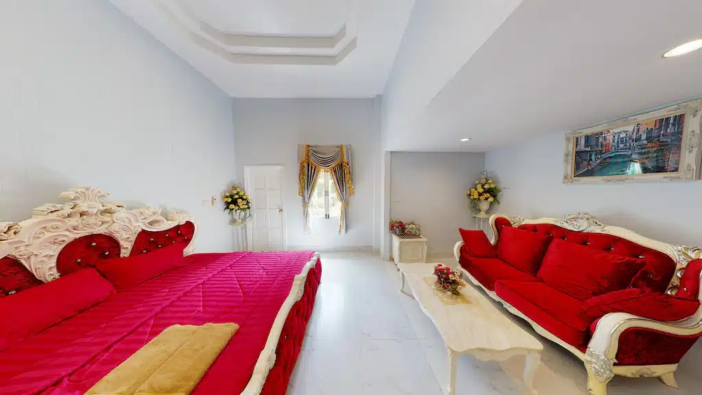 ห้องนอนสีขาวที่รีสอร์ททองผาภูมิมีเตียงสีแดงสไตล์บาร็อค โซฟาสีแดงที่เข้ากัน โต๊ะกาแฟ ผ้าม่านหรูหรา ที่พักทองผาภูมิ การจัดดอกไม้ และภาพวาดบนผนัง