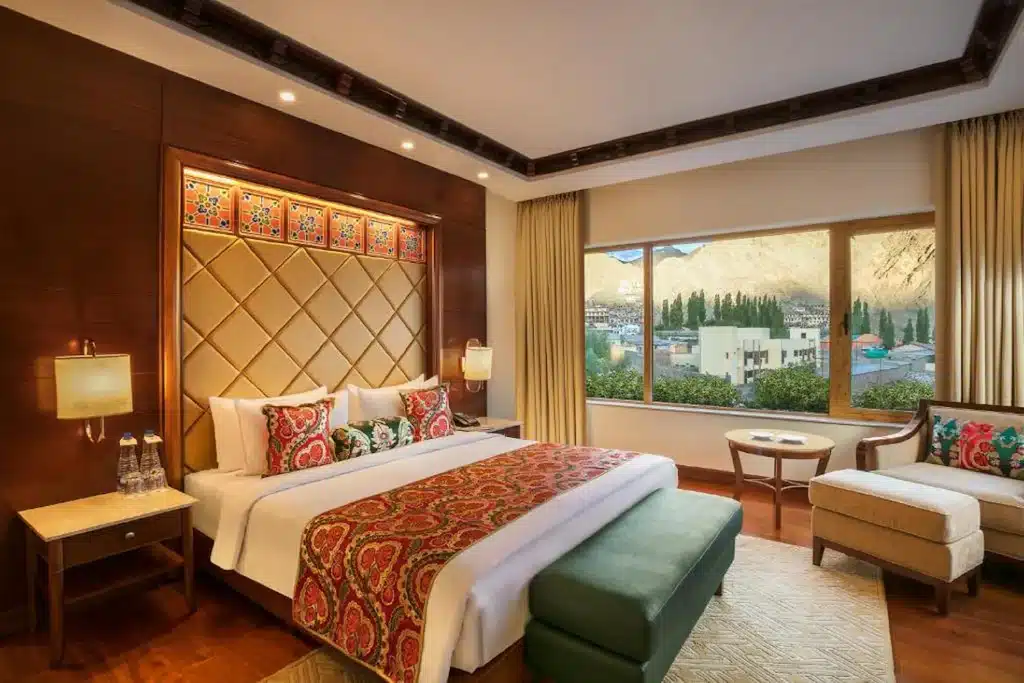 ห้องพักหรูในโรงแรมพร้อมเตียงขนาดใหญ่ ชุดเครื่องนอนที่มีลวดลาย ผนังไม้ และหน้าต่างมองเห็นวิวภูเขาในจังหวัดราชบุรี