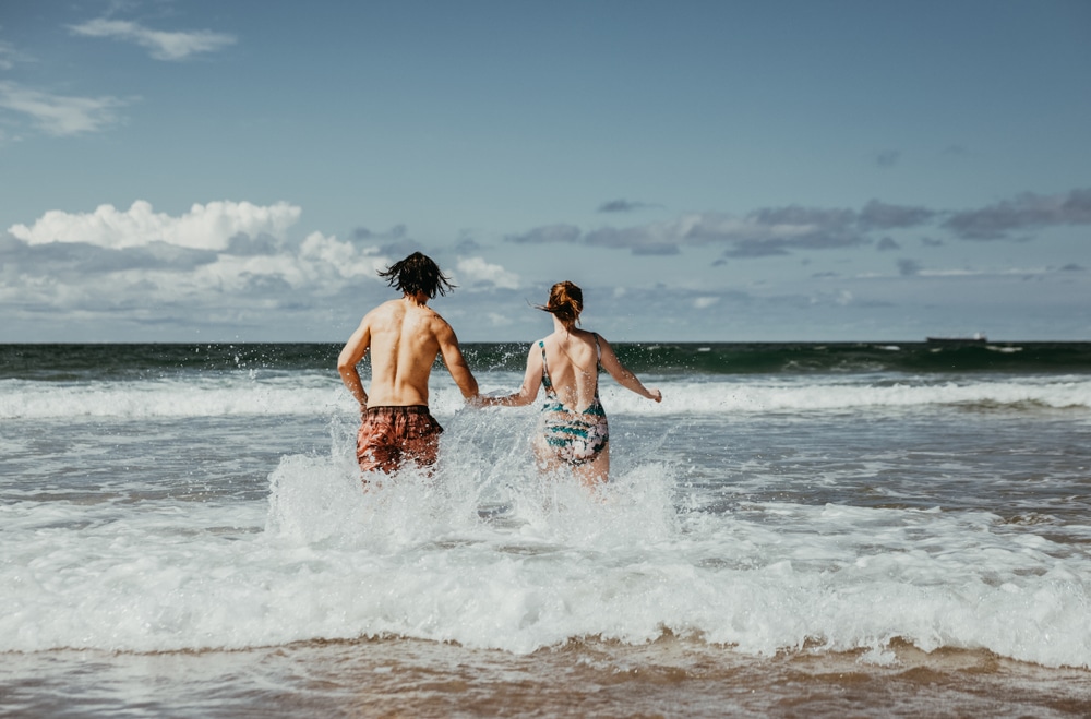 คนสองคนจับมือกันวิ่งไปในเกลียวคลื่นในวันที่อากาศสดใสที่ทะเลในทะเลแคริบเบียน ทะเลที่สวยที่สุดในโลก