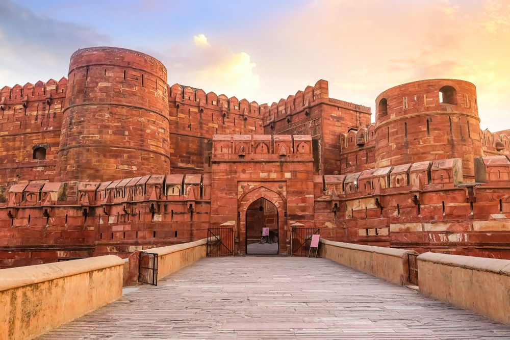 มุมมองจากมุมสูงของทางเข้าป้อมอัคราในอินเดียในช่วงพระอาทิตย์ตก แสดงให้เห็นกำแพงหินทรายสีแดงอันยิ่งใหญ่และซุ้มประตู