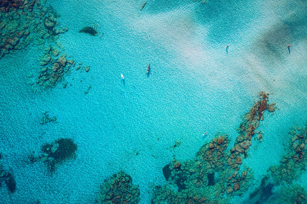 มุมมองทางอากาศของทะเลสีฟ้าครามใสที่มีแนวปะการังกระจัดกระจายและมีเรือลำเล็กๆ ไม่กี่ลำ แสดงให้เห็นทะเลในทะเลในโลก ทะเลที่สวยที่สุดในโลก