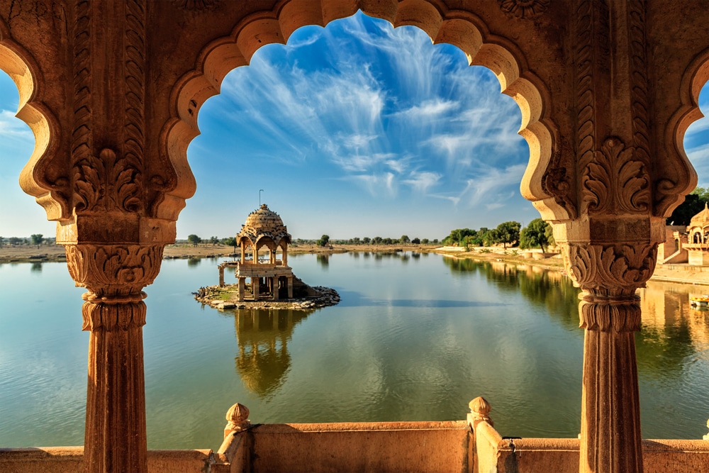 วิวจากซุ้มประตูหินอันวิจิตรมองเห็นทะเลสาบอันเงียบสงบ โดยมี Rajasthani chhatri (อนุสาวรีย์) แบบดั้งเดิมอยู่ตรงกลาง ใต้ท้องฟ้าสีคราม