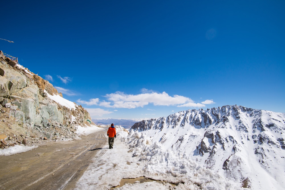 คนใส่แจ็กเก็ตสีแดงเดินไปตามถนนบนภูเขาหิมะที่ราชบุรีใต้ท้องฟ้าสีครามสดใส