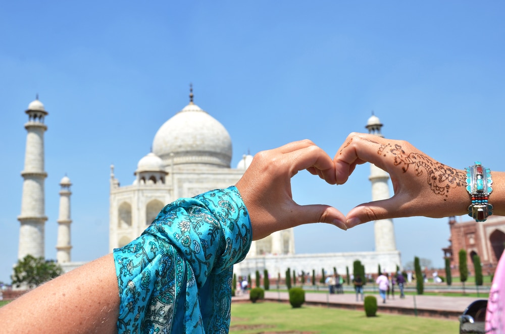 มือเป็นรูปหัวใจหน้าทัชมาฮาล มือข้างหนึ่งตกแต่งด้วยลวดลายเฮนน่า สื่อถึงแก่นแท้ของเที่ยวอินเดีย