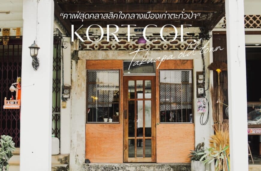         มุมมองถนนของหน้าร้านที่มีป้าย "KORT COE Tatanga เมืองเก่า" ด้านหน้าอาคารมีประตูไม้และของประดับตกแต่งอันหรูหรา ข้อความภาษาไทย ได้แก่ "โอ้เล่ง คาเฟ่ตะกั่วป่า" ปรากฏเหนือป้ายหลัก