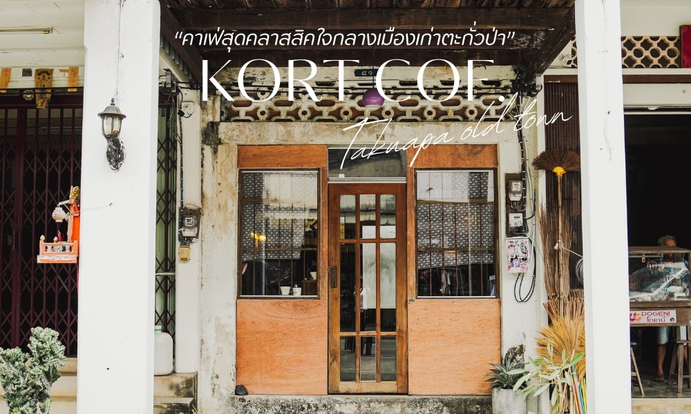 มุมมองถนนของหน้าร้านที่มีป้าย "KORT COE Tatanga เมืองเก่า" ด้านหน้าอาคารมีประตูไม้และของประดับตกแต่งอันหรูหรา ข้อความภาษาไทย ได้แก่ "โอ้เล่ง คาเฟ่ตะกั่วป่า" ปรากฏเหนือป้ายหลัก