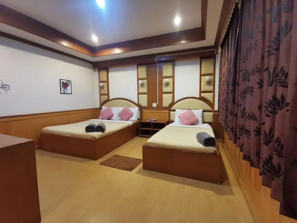 ห้องพักโรงแรมในน่านมีเตียงเดี่ยว 2 เตียงที่จัดอย่างประณีต ตกแต่งด้วยไม้ โต๊ะเล็กๆ ระหว่างเตียง และหน้าต่างบานใหญ่พร้อมผ้าม่านสีเข้ม มีผ้าเช็ดตัววางไว้ที่ปลายเตียงแต่ละเตียง จึงเป็นฐานที่สมบูรณ์แบบสำหรับการท่องเที่ยวเชิงผจญภัยของคุณ