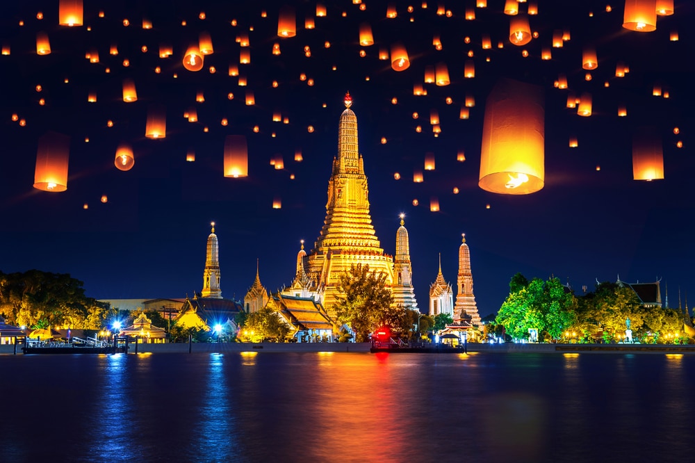 โคมลอยส่องสว่างท้องฟ้ายามค่ำคืนเหนือวัดอรุณในกรุงเทพฯ ประเทศไทย ในช่วงเทศกาลงานลอยกระทง สะท้อนอย่างสวยงามเหนือแม่น้ำเจ้าพระยา งานลอยกระทง
