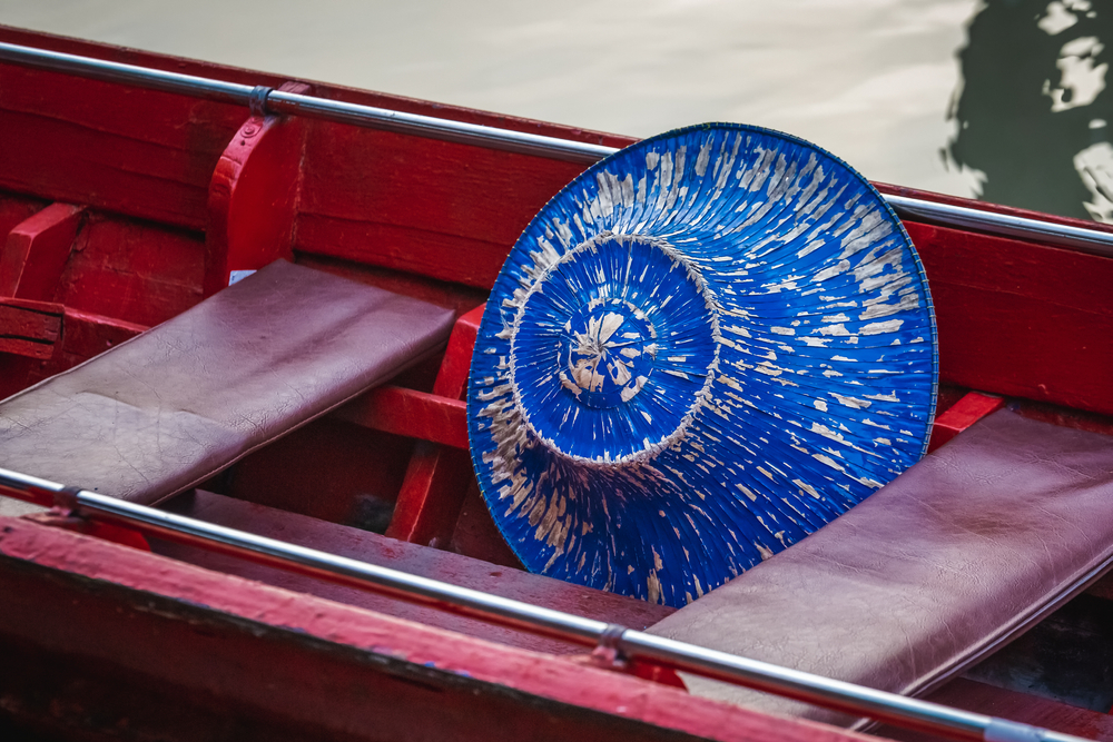หมวกทรงกรวยสีน้ำเงินมีจุดสีขาววางอยู่บนเบาะเรือไม้สีแดงที่ตลาดน้ำพัทยา ตลาดน้ำพัทยา 